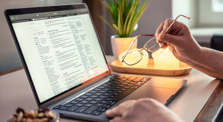 Persona sosteniendo sus lentes mientra revisa las facturas en el portátil Profitline