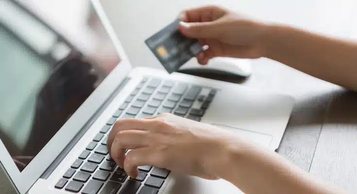 Persona sujetando su tarjeta de crédito mientras usa un portatil